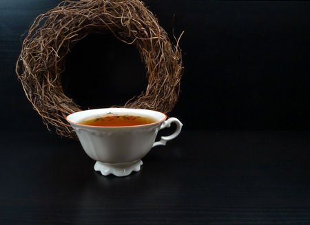 Hot tea cup porselain with wicker wreath at black wooden backgroundの写真素材