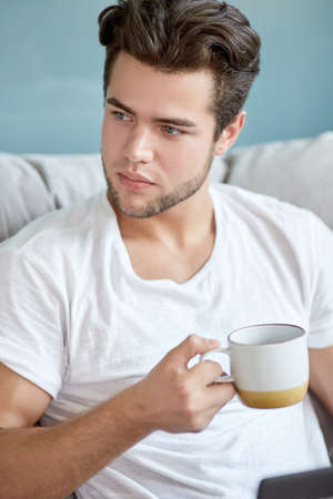 attractive young man sitting in a comfortable chair with a cup of coffe, front view. work in a modern office. Portrait of business startups. handsome guy with the coffe cup.の写真素材
