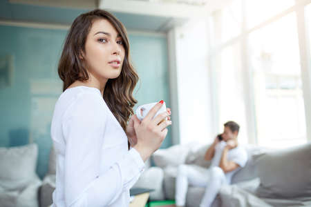 Coffee makes her day. Young handsome woman drinking coffee and looking to the camera while sitting at her working place. Openspace, co-working, time cafeの写真素材