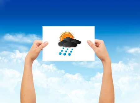 Hand holding a paper with weather sign on landscape blue sky backgroundの写真素材