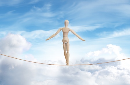 Wooden model standing on a rope over the cloud skyの写真素材