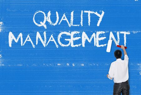 Man painting word on cement texture wall background, Quality Managementの写真素材