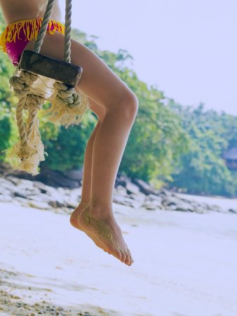 Legs of  caucasian girl, child, kid  on swing at the trpoical beachの写真素材