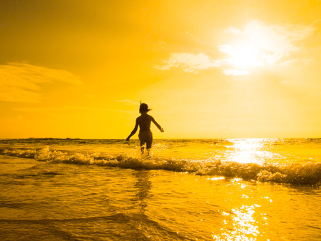Silhouette of girl standing on beach at the orange sunset.の写真素材