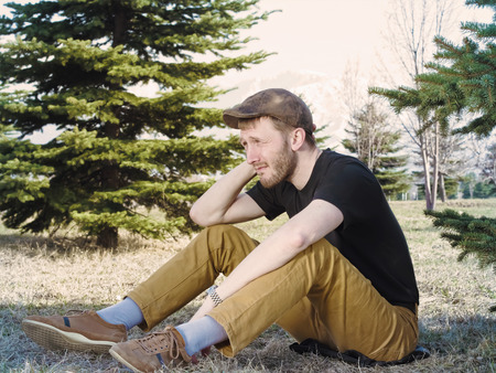 Young caucasian man reflects and sitting in meadow between firs at springの写真素材