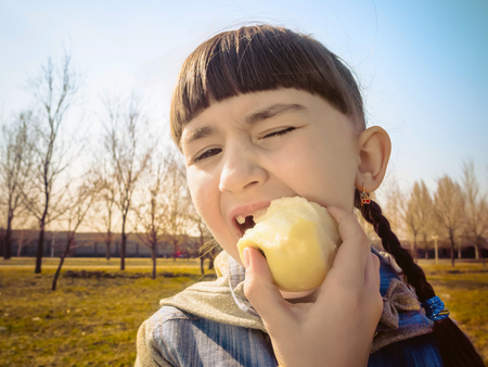 Portrait of young caucasian girl eating apple at park outdoorsの写真素材