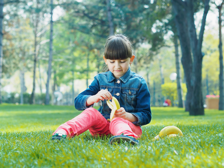 Portrait of nice caucasian girl kid clean fresh banana in summer outdoorsの写真素材