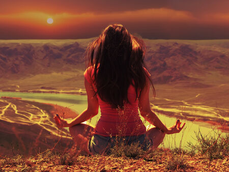 Portrait of young caucasian beautiful sport  women sitting at lotus pose at sunset background of river in red shirt and blue pantsの写真素材