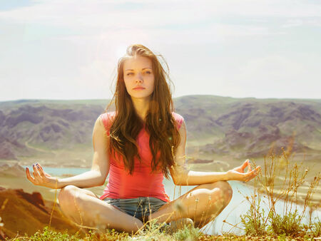 Portrait of young caucasian beautiful sport  women sitting in lotus pose at sunlight background of river in red shirt and blue pantsの写真素材