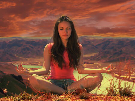 Portrait of young caucasian beautiful sport  women sitting in lotus pose at sunset background of river in red shirt and blue pantsの写真素材