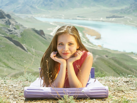 Portrait of young caucasian beautiful sport women lying on travel mat  in summer nature on the background of riverの写真素材