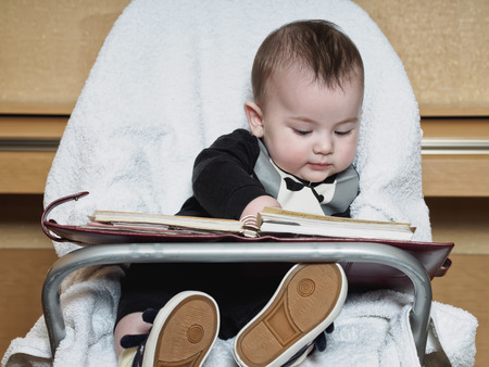 Small caucasian baby sitting in chear with notepadの写真素材