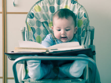 Small caucasian baby sitting in chear with notepadの写真素材