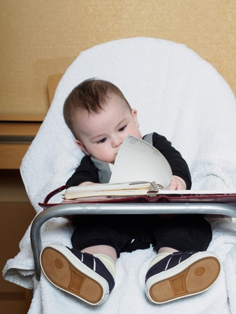 Small caucasian baby sitting in chear with notepadの写真素材