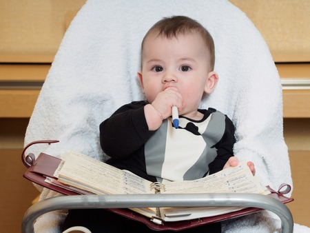 Small caucasian baby sitting in chear with notepadの写真素材