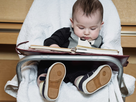 Small caucasian baby sitting in chear with notepadの写真素材