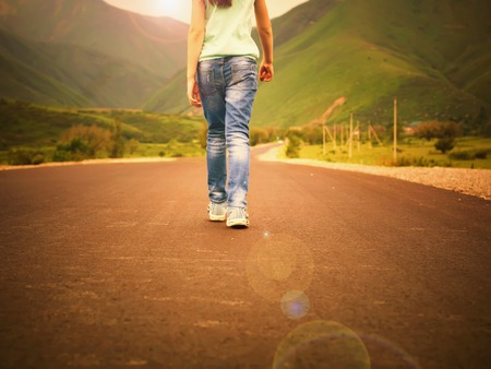 Little girl child walking on road to mountains at sunset outdoorの写真素材