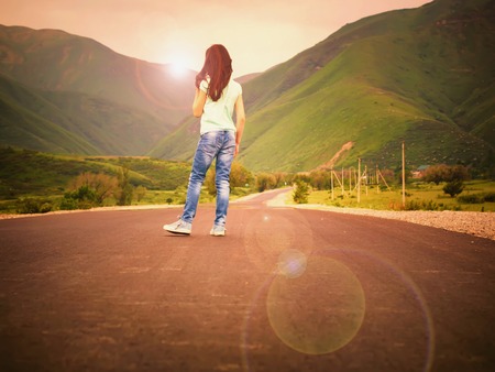 Little girl child walking on road to mountains at sunset outdoorの写真素材