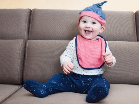 Caucasian baby boy weared bib sitting on brown sofa at homeの写真素材