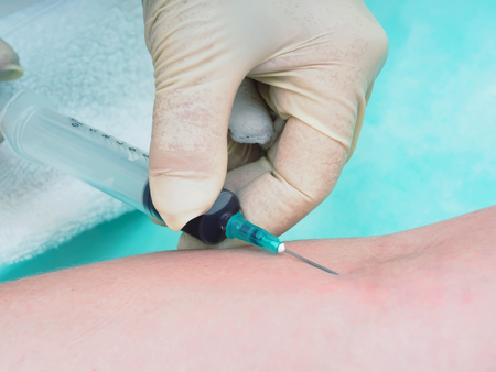 Doctor drawing blood from female patient's arm in examination roomの写真素材