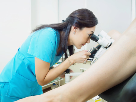 Asian woman gynecologist examining patient in hospital using a colposcope