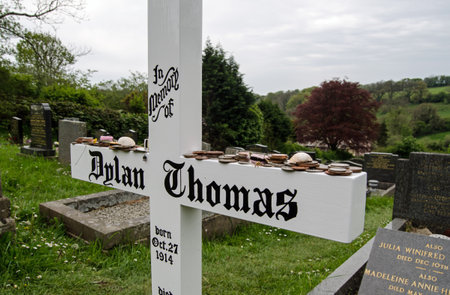 LAUGHARNE, UK - MAY 5, 2014  Simple wooden cross marking the grave of the great Welsh poet Dylan Thomas in Laugharne, South Wales   Cockle shells, coins and sweets have bee placed as reminders of his literature のeditorial素材