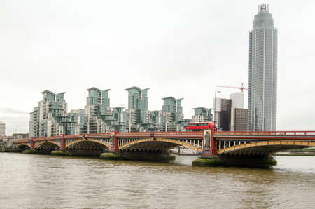 View of a red bus travelling over Vauxhall Bridge on a cloudy morning in London.