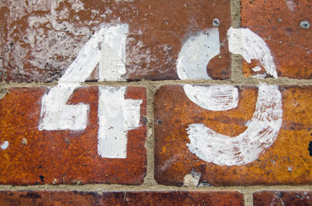 A number 49 painted on the exterior of a glazed brick wall.  Viewed from pavement, London.のeditorial素材