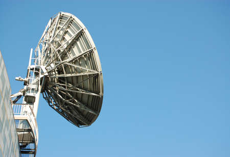 A large, industrial satellite dish used in the communications industy against a blue sky on a sunny, summer day with space for copy.の写真素材