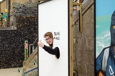 WESTON-SUPER-MARE, UK - AUGUST 26, 2015:  A visitor makes use of the selfie-hole parody of a traditional seaside photo opportunity at Dismaland in Weston-Super-Mare Somerset.  The Somerset resort has become very popular thanks to the work of Banksy and otのeditorial素材