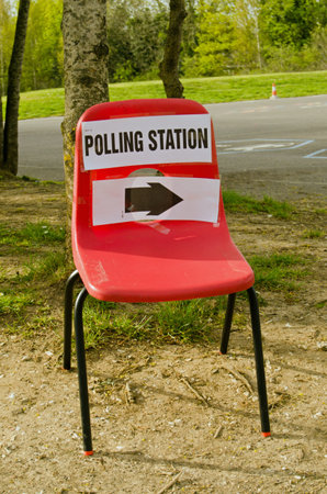 A small child's stacker chair with a sign pointing towards a polling station at a primary school on election day in Basingstoke, Hampshire, UK.のeditorial素材