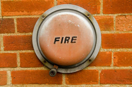 An old fashioned hand operated fire alarm bell fixed the brick wall of the exterior of a building.の写真素材