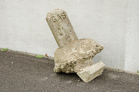 A street marker for a gas main broken and lying in the road like a broken headstone.