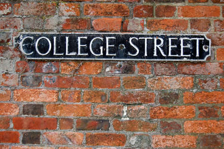 An old, cast iron road sign for 'college street' on a warm orange brick wall. Winchester, Hampshire