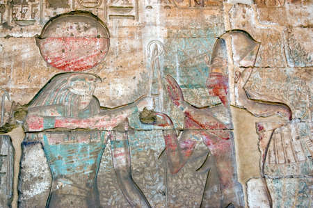 An ancient egyptian hieroglyphic carving showing the falcon headed god Horus with the Pharoah Ramses II before the sacred tree of life. Giant carvings on an outer wall of the Temple to Osiris at Abydos, Egyptの写真素材