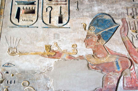 A wonderfully preserved coloured hieroglyphic carving of the Pharoah Ramses II holding a lamp. Ancient Egyptian picture on a wall at the Temple of Medinet Habu on the west bank of the Nile at Luxor, Egypt.の写真素材