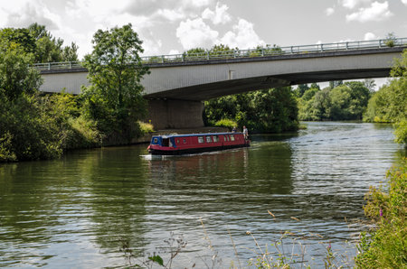 Marlow, UK - July 19, 2021: Two men sailing their narrowboat barge along the River Thames under the Marlow By-Pass on a sunny summer afternoon on the Oxfordshire / Berkshire border.のeditorial素材