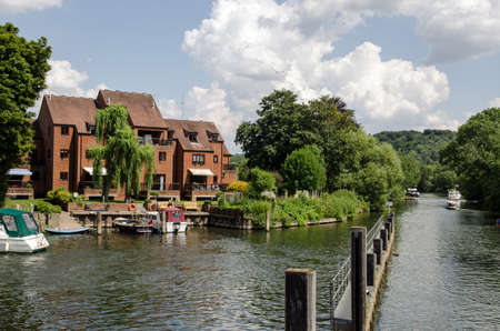 Riverside apartments overlooking the River Thames at Marlow, Buckinghamshire on a sunny, summer afternoon.  Pleasure boats are moored by the bank and others continue downriver towards Maidenhead.の写真素材