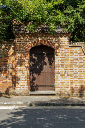 A wooden garden gate in the arch of a brick wall.の写真素材