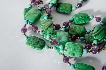 Coils of a handcrafted necklace made with beads of purple amethyst, blue turquoise and green crazy agate beads. Viewed on a white background with drop shadow.の写真素材
