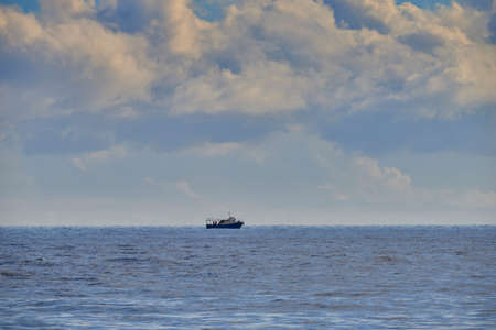 A fishing boat offshore, in the open sea, among the clouds of the skyの写真素材
