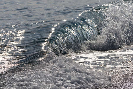detail of backlit sea waves on a sunny day in autumn breaking on the shorelineの写真素材