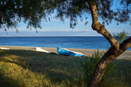 green coast of Eastern Sicily, with two fishing boats and in the background the coast of Calabria in the cloudsの写真素材