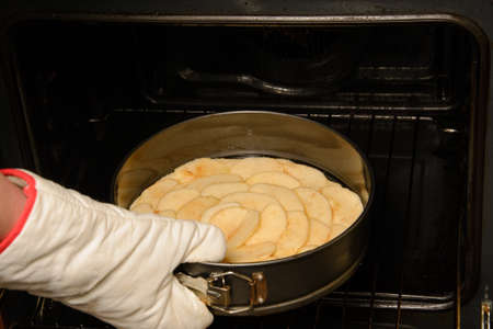 Close up of woman putting apple pie in backing tray inside oven with gloves in her hand