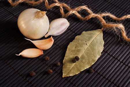 onion, garlic, black pepper and bay leaf on a black tableの写真素材