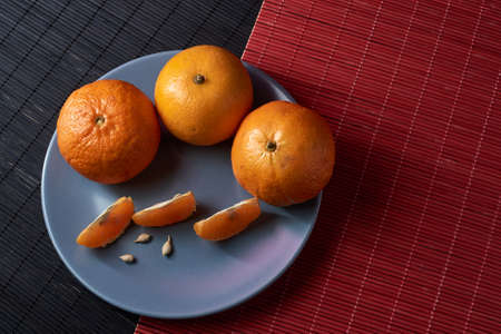 Tangerines with slices in plate on black and red background