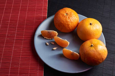 Tangerines with slices in plate on black and red background
