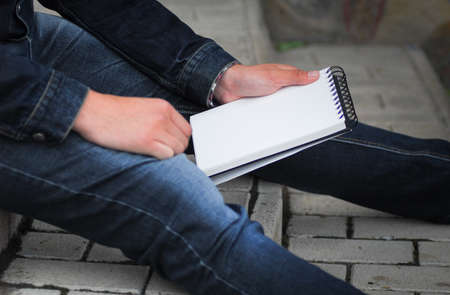 Male hand holding a book and sitting outside mock upの写真素材