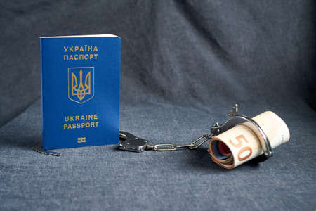 Ukrainian biometric passport and handcuffs with money on the tableの写真素材
