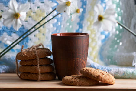 Brown cup and large biscuits with sesame, flax and sunflower seeds with flowers on wooden table and...